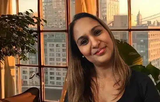 Farhana Sonday, specialist physiotherapist at PhysioReform London, smiling indoors near window