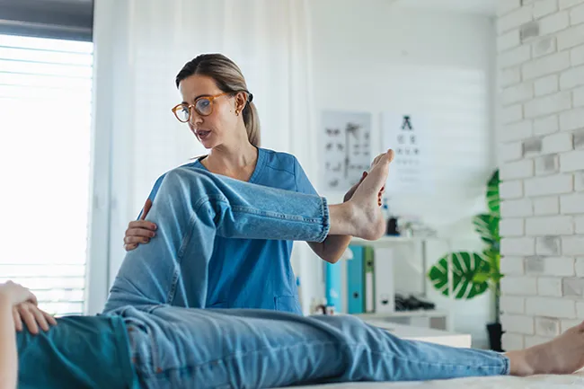 Physiotherapist supporting a patient during post-operative leg rehabilitation in a Central London clinic