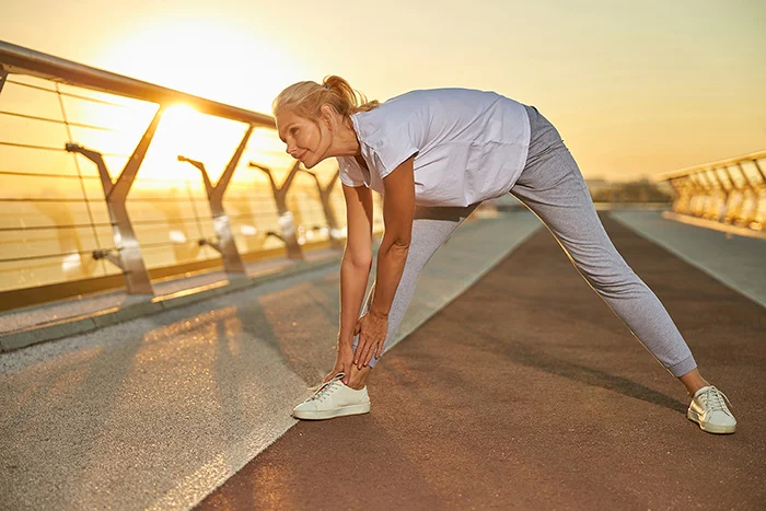 Woman stretching outdoors at sunrise to reduce joint stiffness during cold weather
