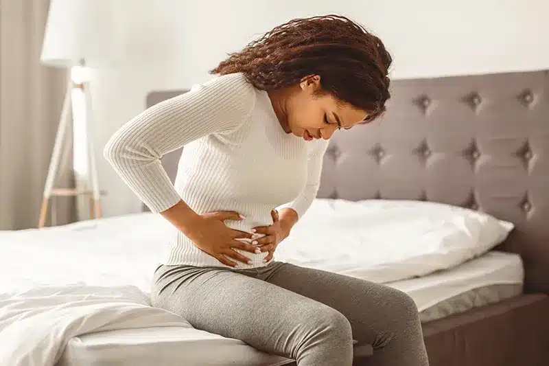 Woman experiencing pelvic pain sitting on a bed, representing tight pelvic floor symptoms and pelvic pain